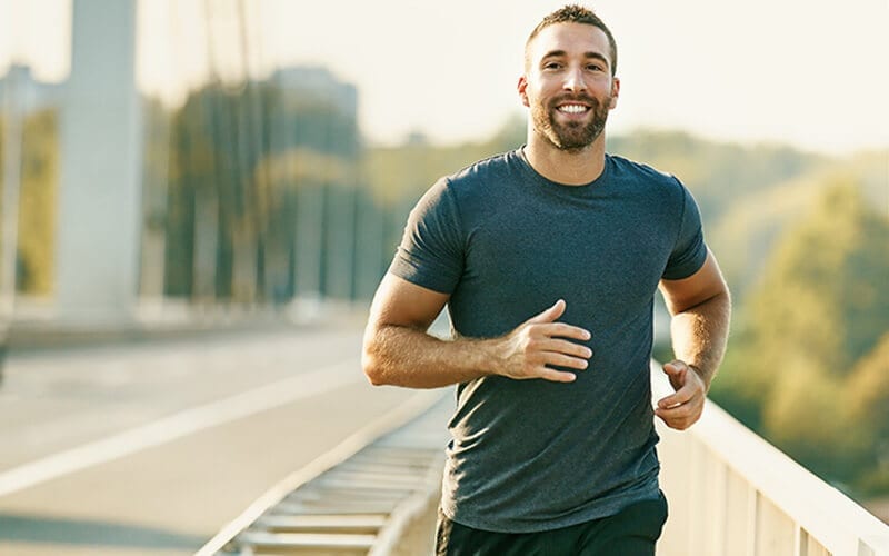 A smiling athletic man jogging across a bridge.