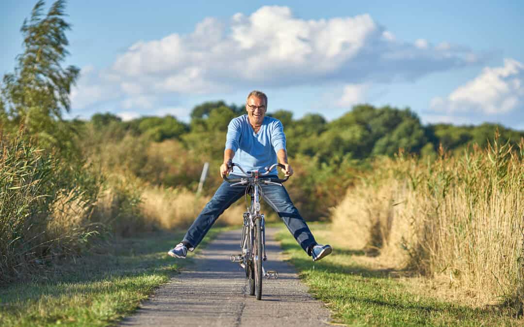 A man riding a bike down a bike lane in a field. Both feet are splayed out.